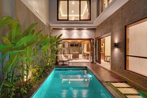 A modern outdoor pool area with a wooden deck, lounge chairs, and a glass-enclosed dining area. - Villa Queeno - Nusa Dua (Nusa Dua)