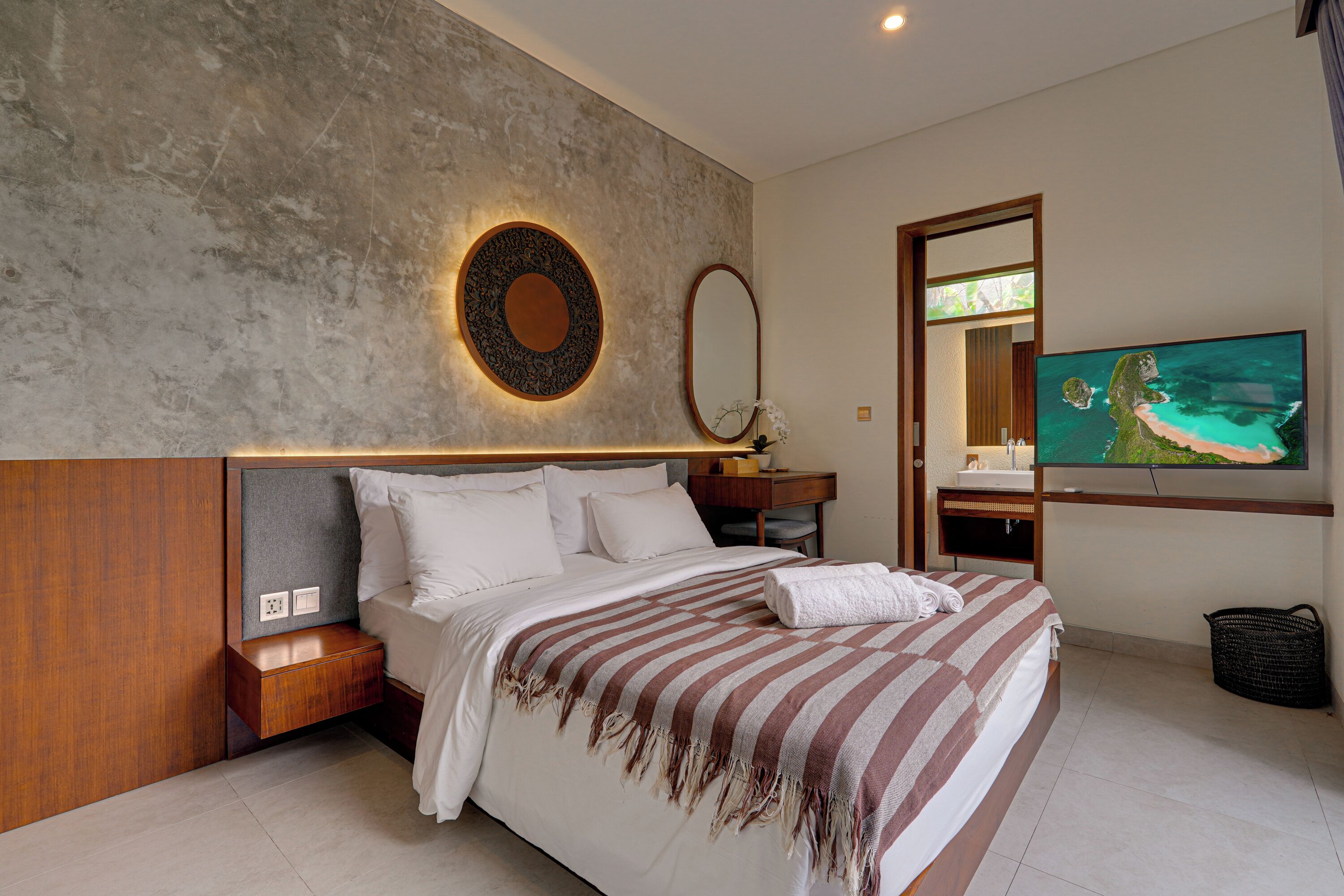 A modern bedroom with a large bed, a TV, and a bathroom with a sink and mirror.