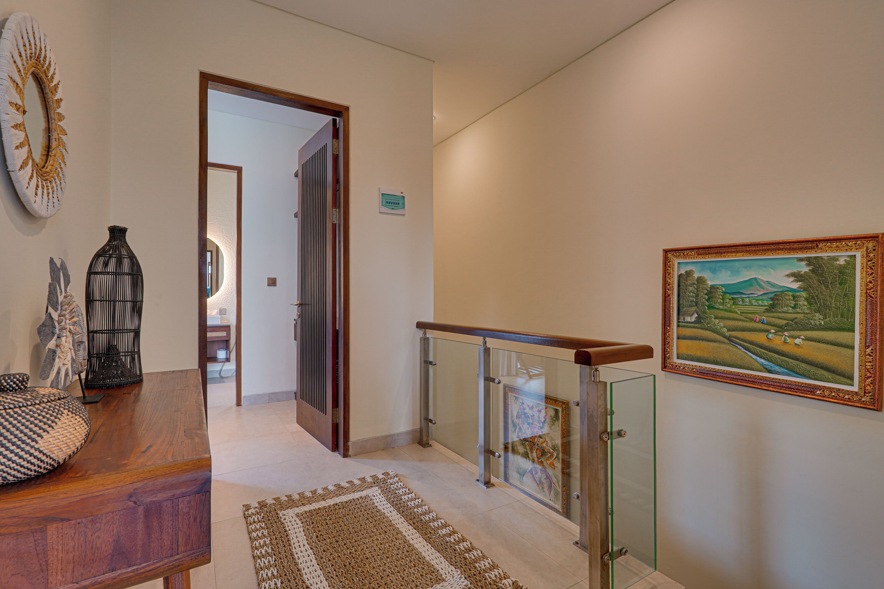 Um corredor com escrivaninha de madeira, tapete de crochê, guarda-corpo de vidro e um quadro emoldurado.