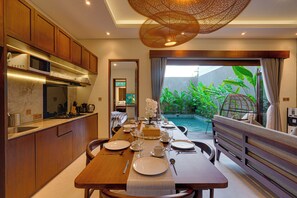 A modern kitchen with wooden cabinets, a built-in microwave, and a dining area with a table set for four. - Villa Queeno - Nusa Dua (Nusa Dua)