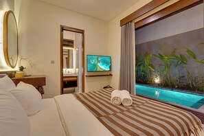A hotel room with a bed, a television, a small bathroom, and a view of a pool. - Villa Queeno - Nusa Dua (Nusa Dua)