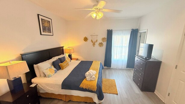 A bedroom with a bed, bedside tables, a ceiling fan, a TV, and a wardrobe. - 6025 Rookery 3 The Real Place (Gulf Shores)