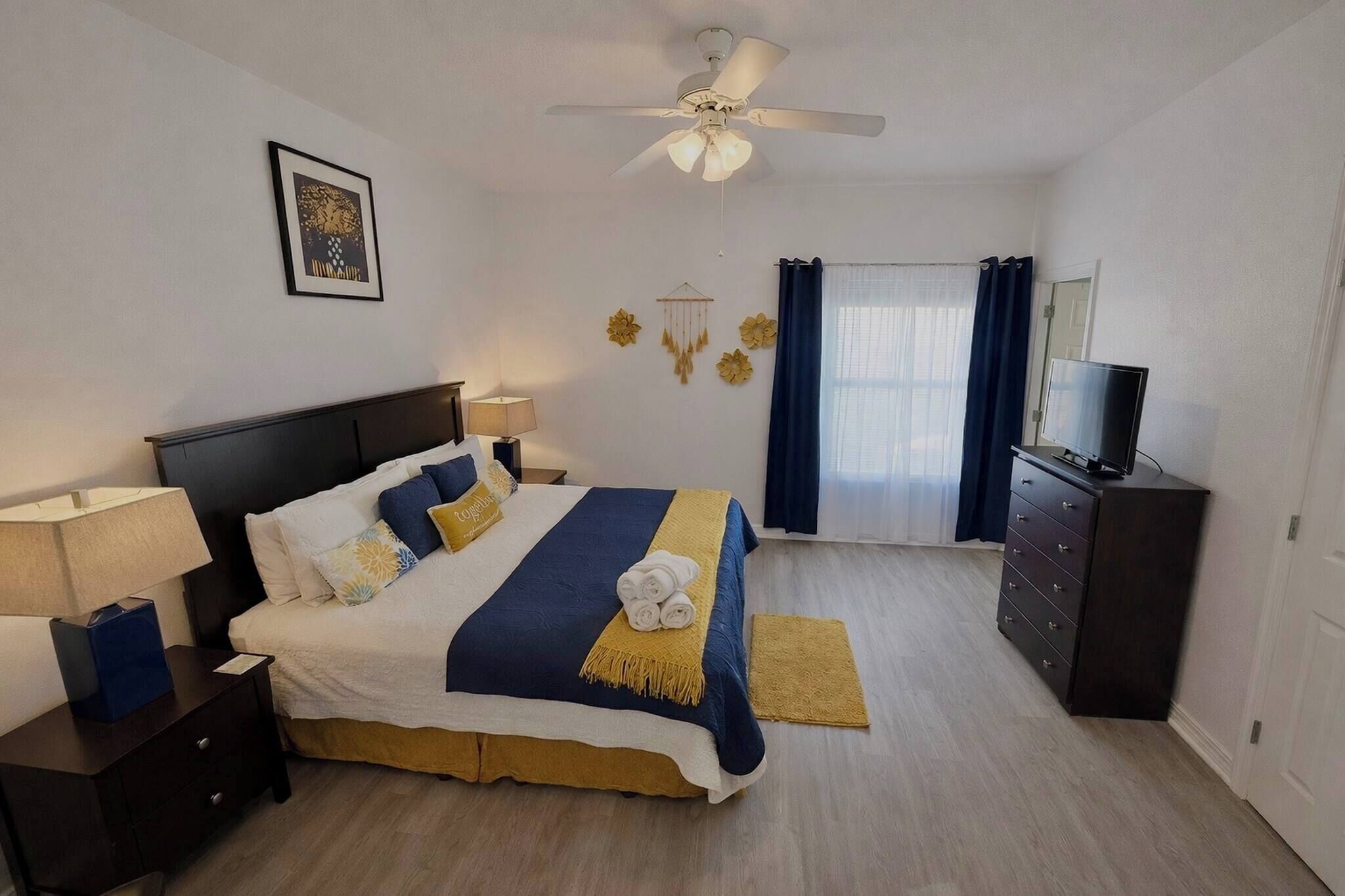 A neatly arranged bedroom with a bed, bedside tables, a dresser, a ceiling fan, and a television.