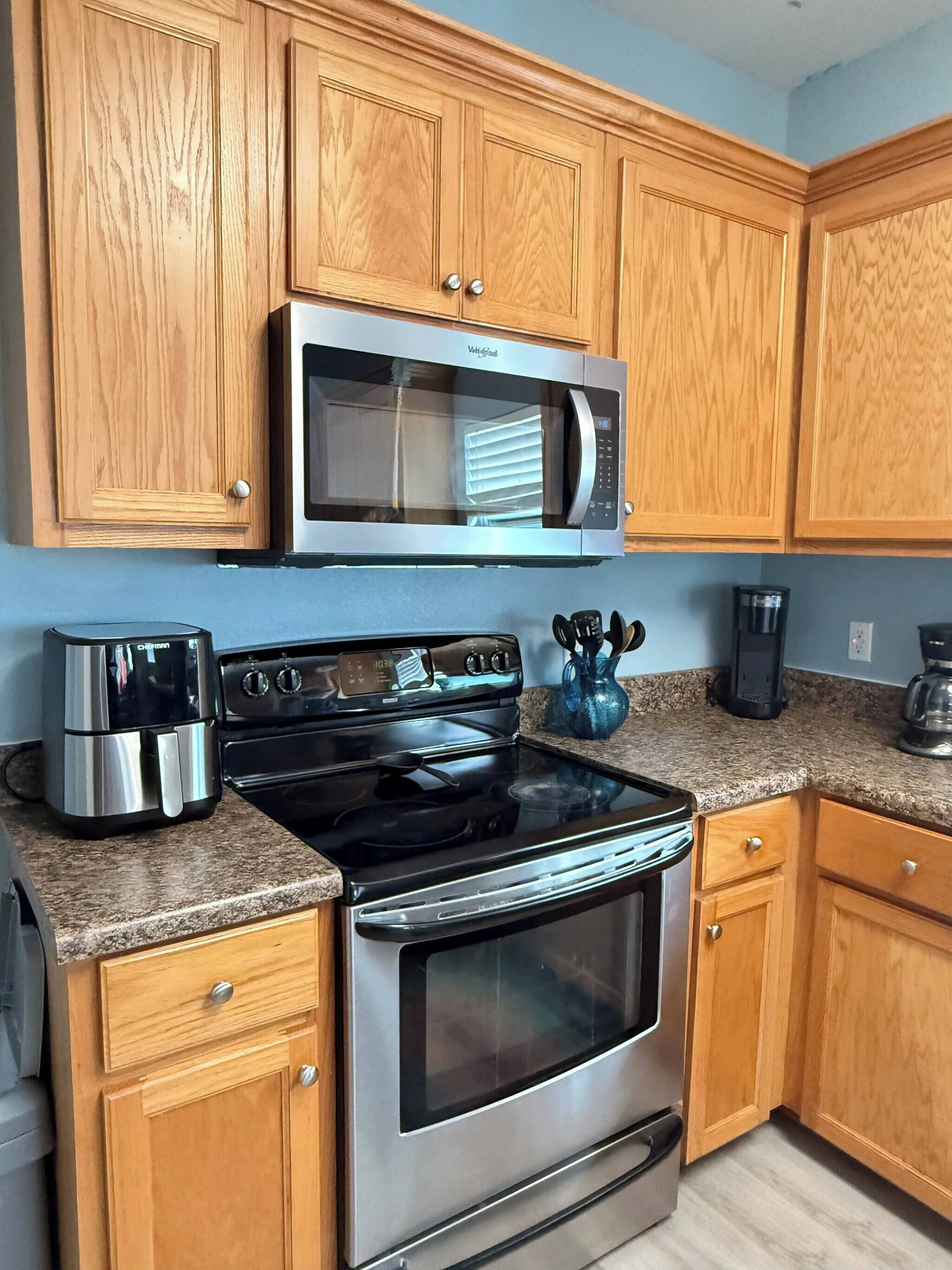 A kitchen with wooden cabinets, a stainless steel microwave, a stove, and a coffee maker.