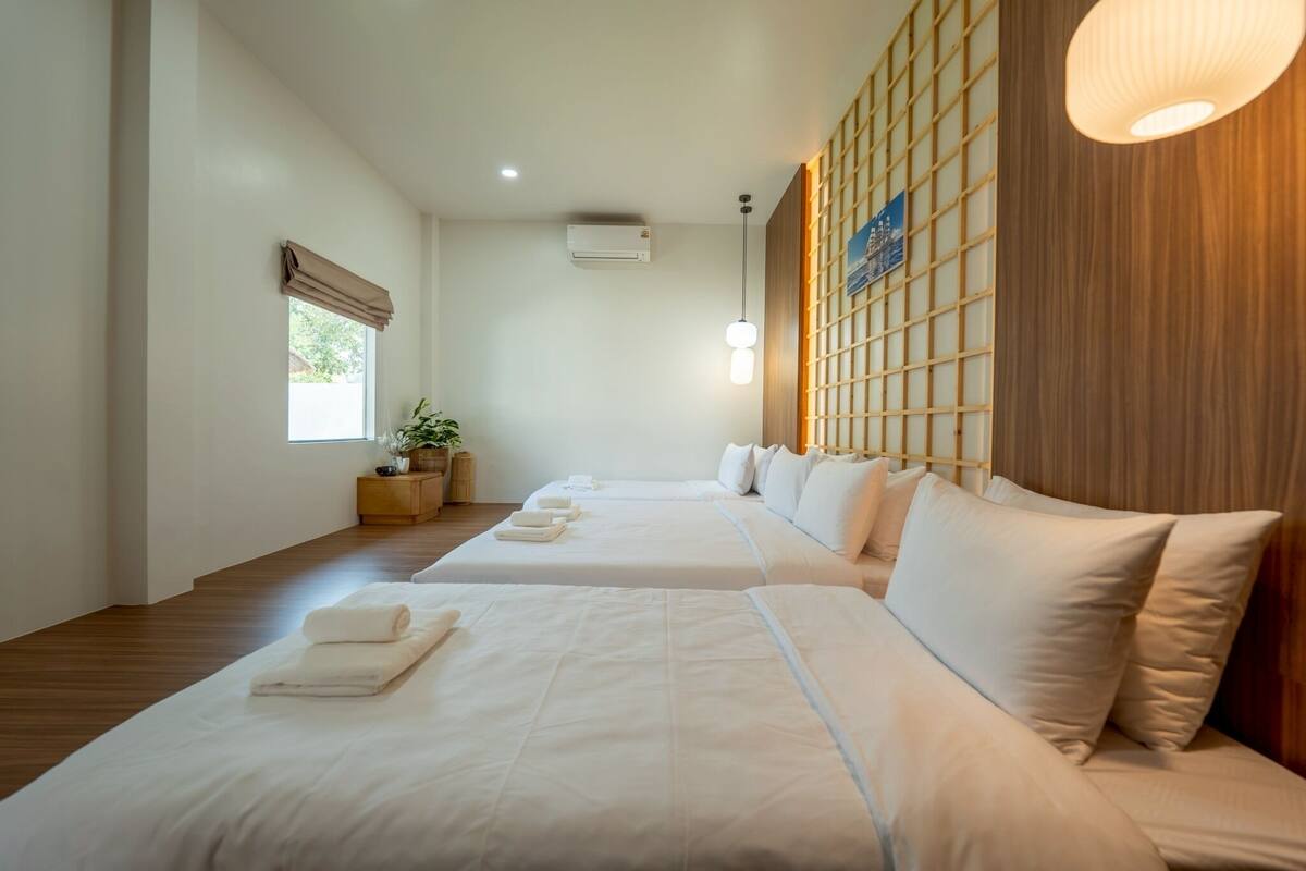 Ein Hotelzimmer mit zwei Betten, Holzboden, einem Fenster mit Aussicht, einer Wand-Klimaanlage und einem Topf mit Pflanze.