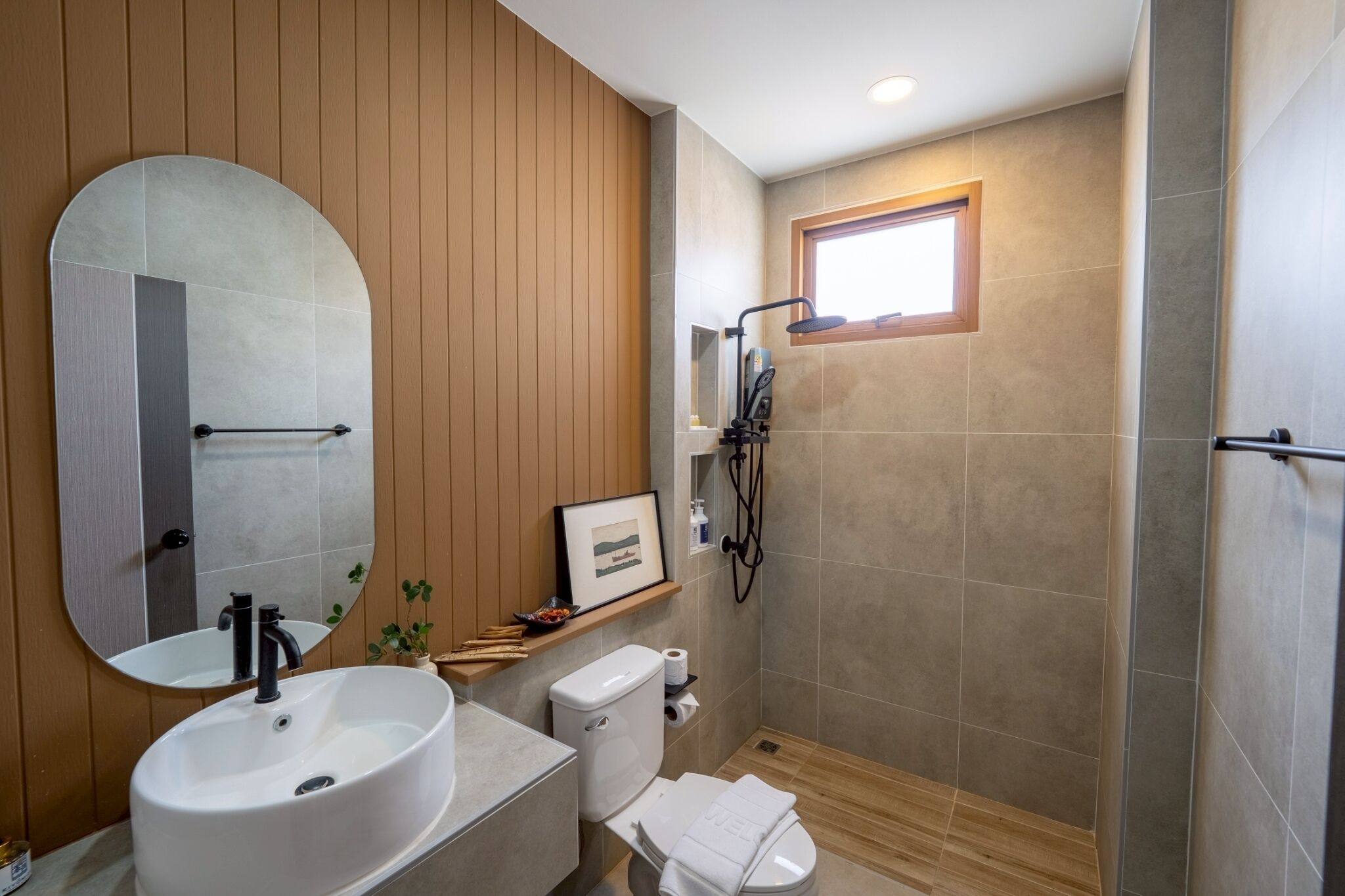 Un baño moderno con un espejo ovalado grande, un lavabo blanco, un inodoro y una zona de ducha.