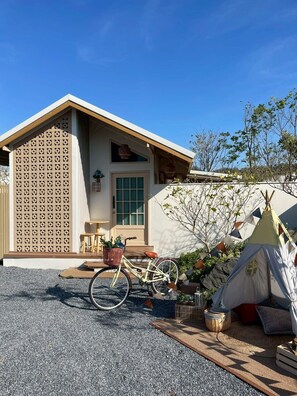 Une maison moderne avec un vélo garé devant, une tente et une clôture en bois.