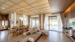 A spacious living area with a wooden ceiling, a sofa, a dining table with chairs, and large windows with curtains. - Kiyomizu Onsen &Glamping Resort Saraburi (Nong Khae)