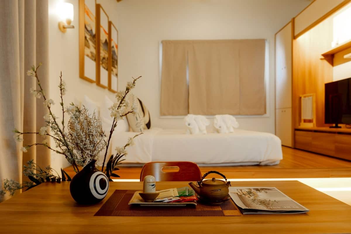 Ein Hotelzimmer mit einem Bett, einem Nachttisch mit Blumenvase, einem Teekessel und einem Tablett mit Teebeuteln und einer Tasse.