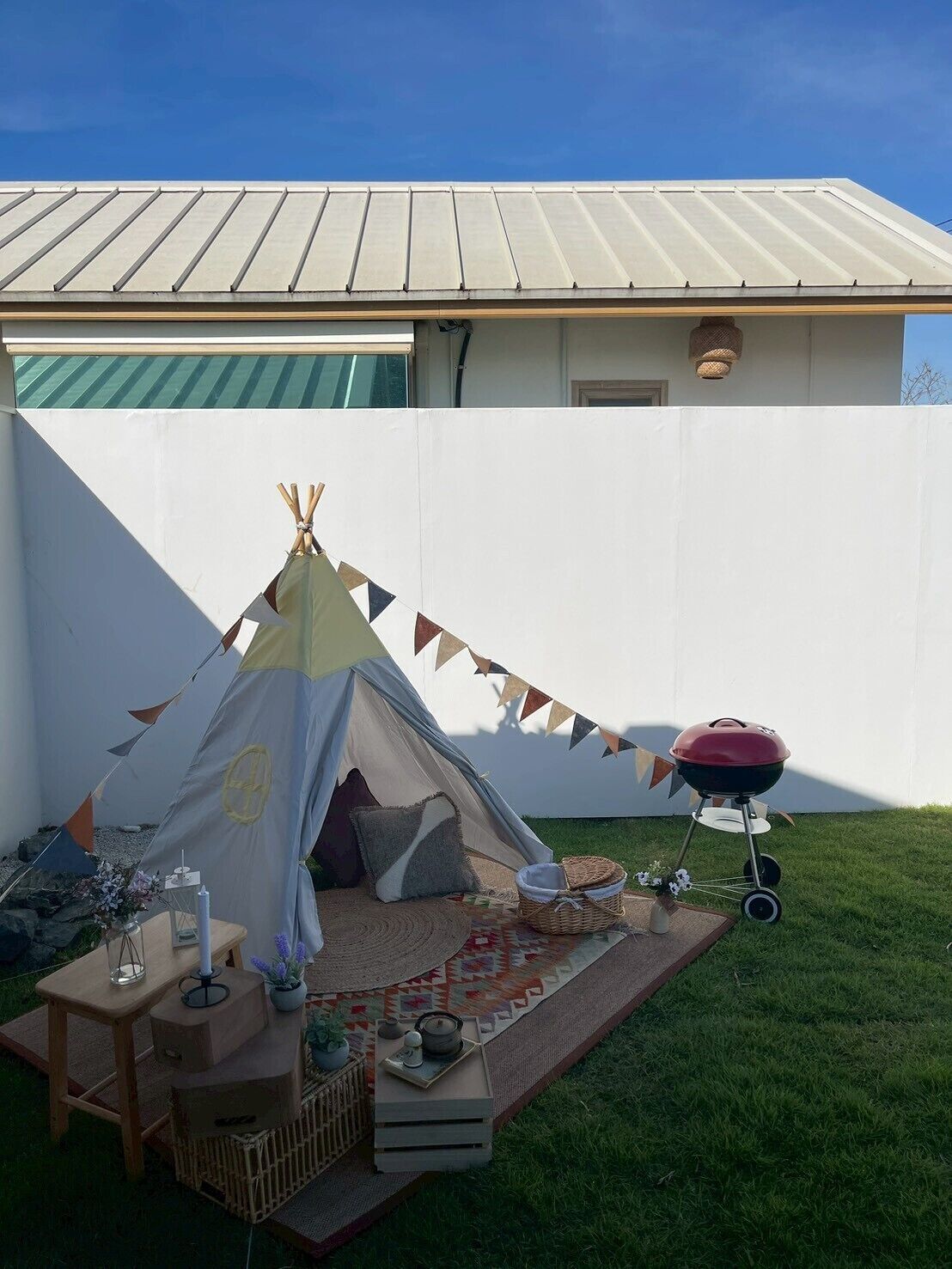A backyard with a teepee, a barbecue, and a picnic setup.