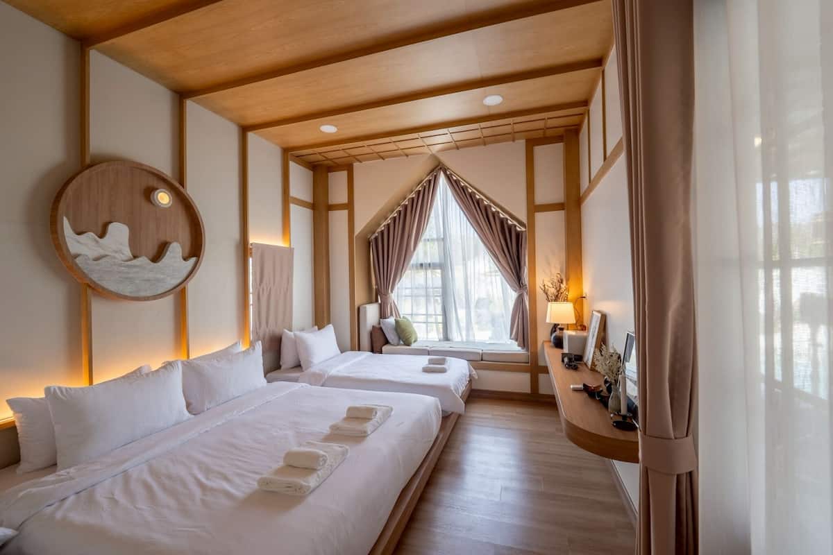 Ein Hotelzimmer mit zwei Betten, einer Holzbalkendecke, einem großen Fenster mit Vorhängen und einem an der Wand hängenden Kunstwerk.