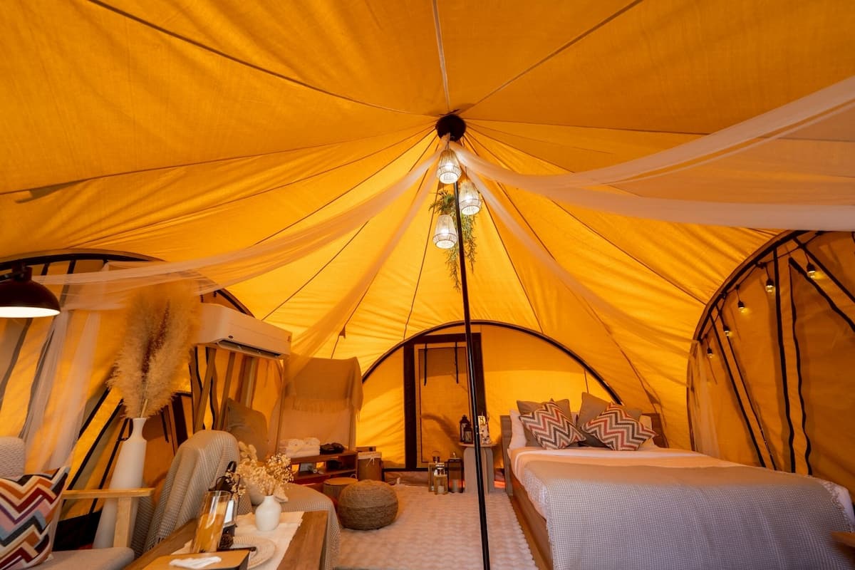 Ein gemütliches Zeltinneres mit Bett, Sitzgelegenheit und einer Hängelampe.
