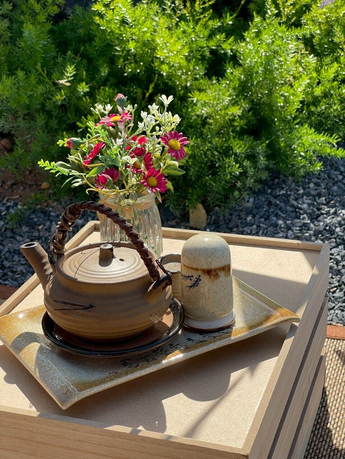 A teapot and cup on a tray with a floral arrangement in the background.