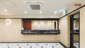 A hotel reception area with a marble counter, a fire safety sign, and a tiled floor. - Amemura Garden Hotel (Osaka)