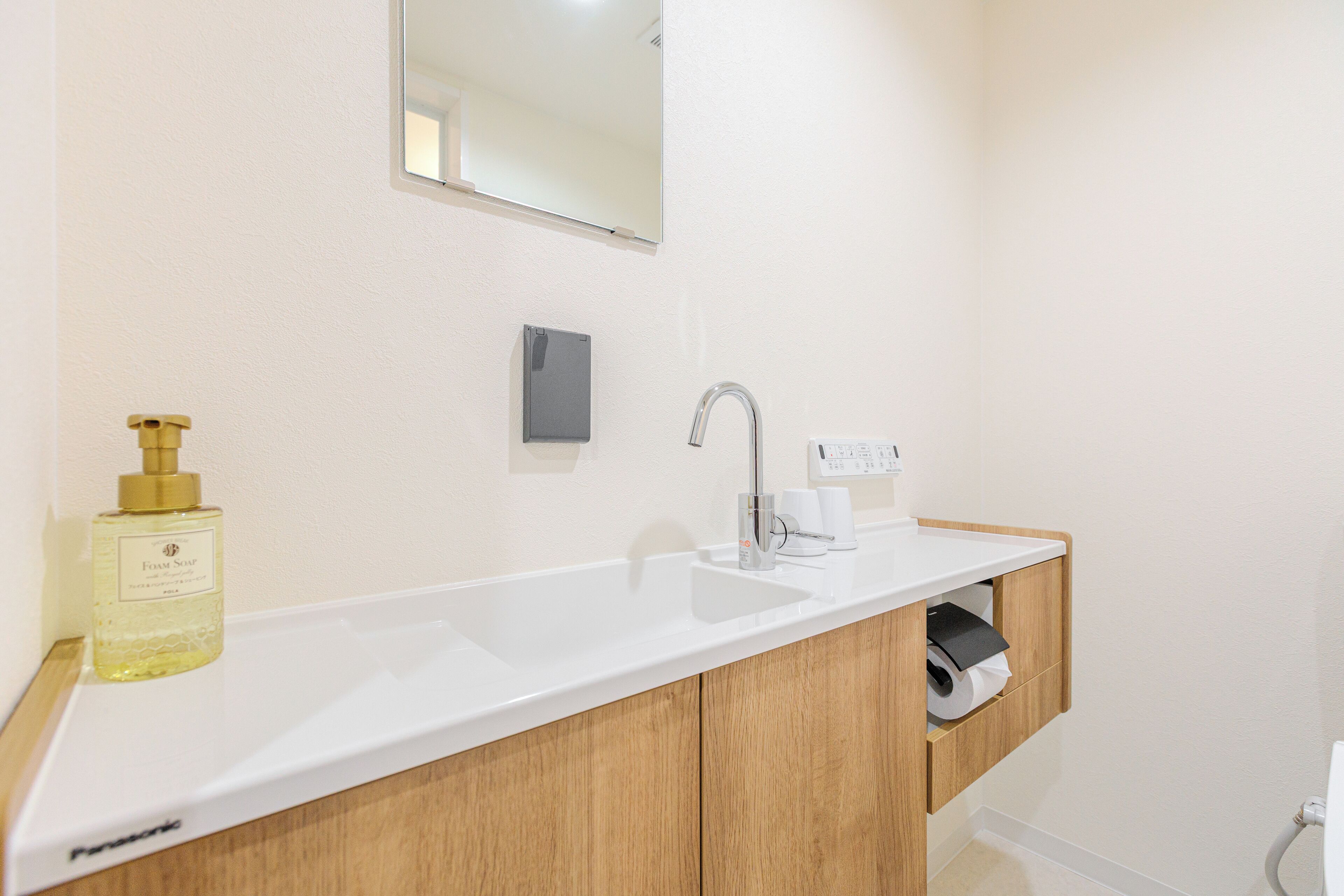 A bathroom with a white sink, wooden cabinets, a mirror, and a bottle of soap.