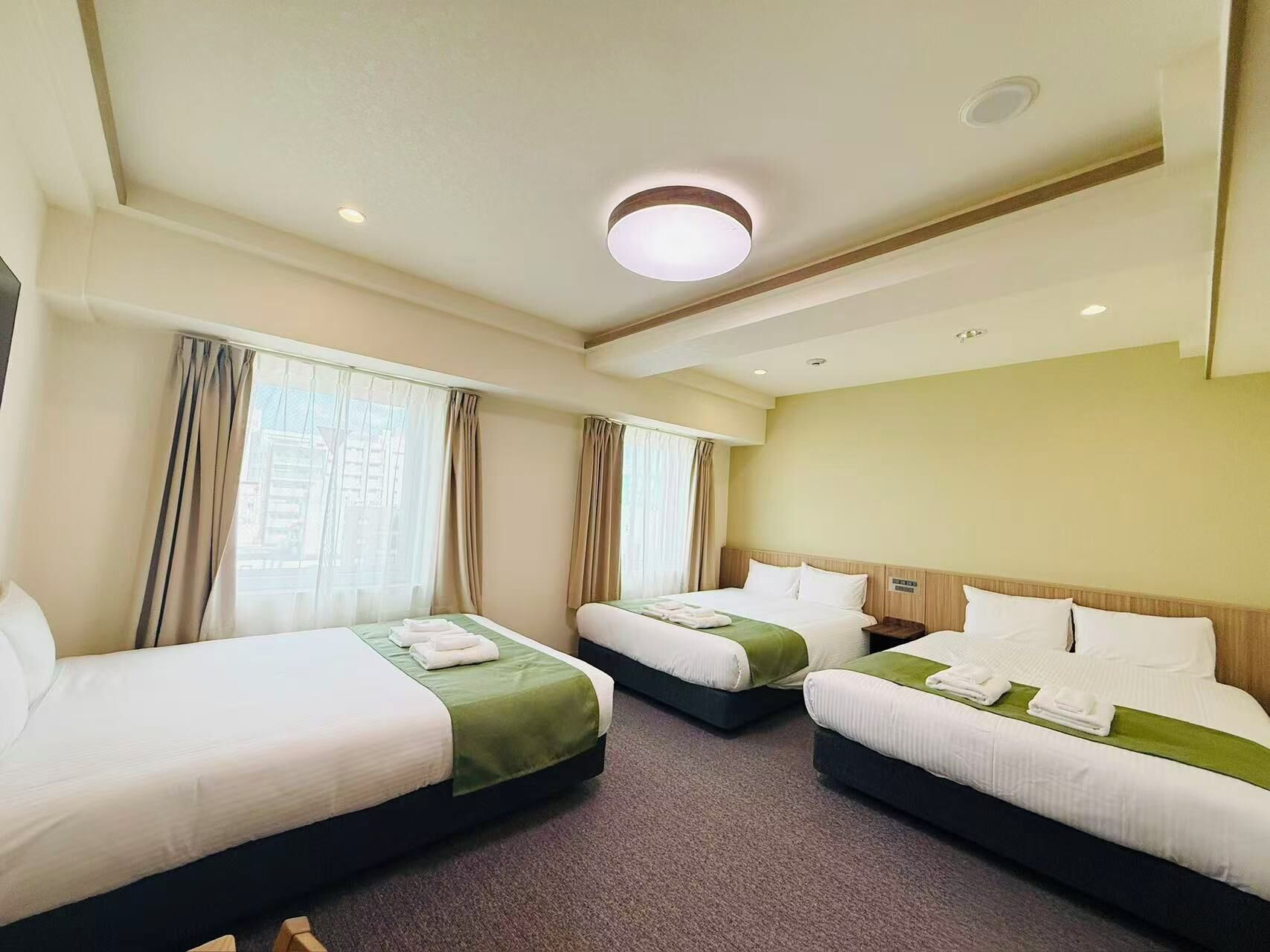 A hotel room with two single beds, a large window, and a ceiling light.