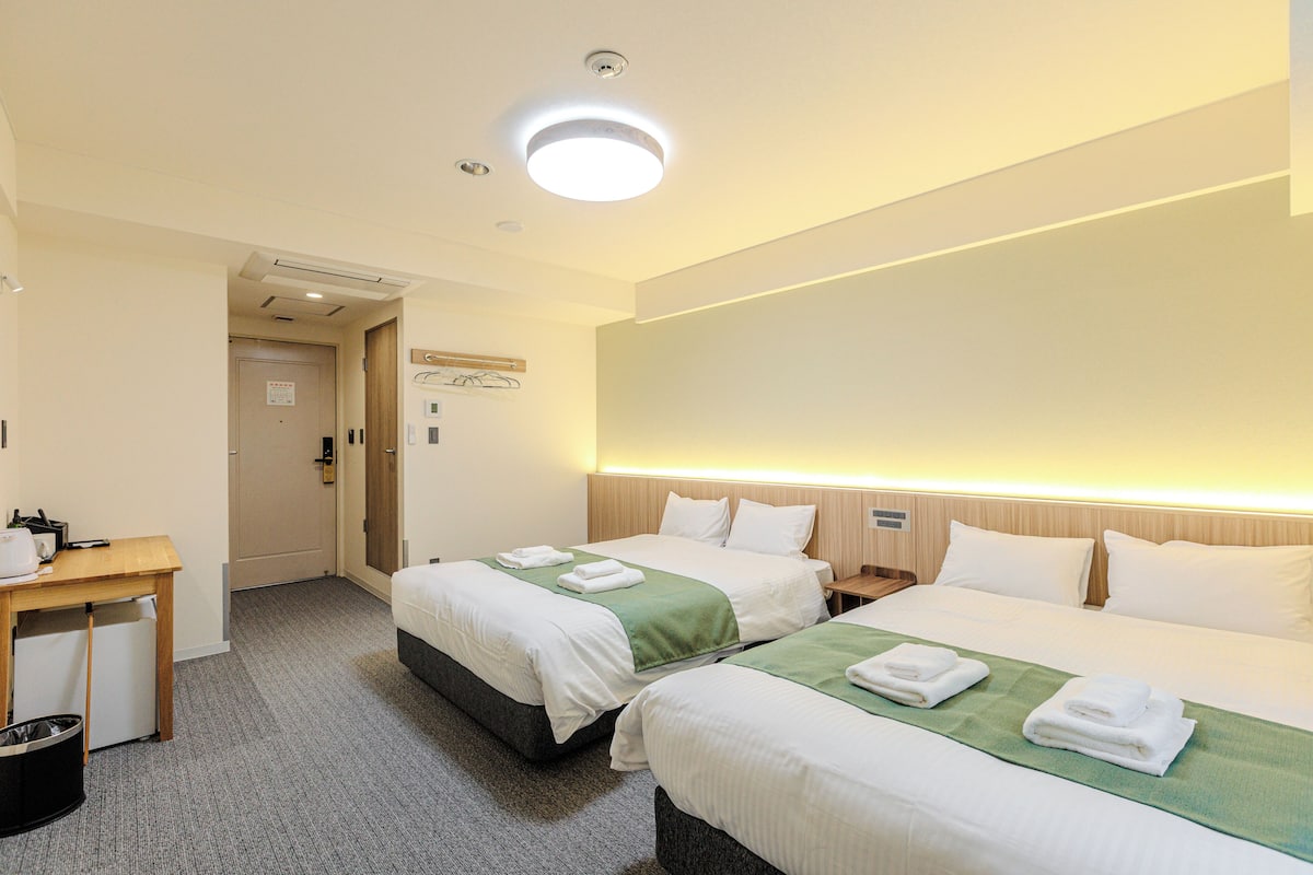 A hotel room with two beds, a desk, and a trash bin.