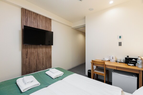 A hotel room with a bed, a desk with a chair, a television mounted on the wall, and a small refrigerator. - Amemura Garden Hotel (Osaka)