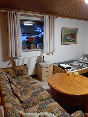 A cozy room with a sofa, a wooden table, a bed, a window with curtains, a radiator, a small cabinet, and a painting on the wall. - Marvelous 2-bedroom apartment in charming Wunstorf perfect for relaxing (Wunstorf)