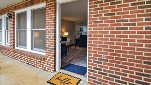 A brick building with a sliding glass door entrance, a visible kitchen area, and a blue mat at the door. - Charming 2BR/2BA Condo - Steps from Auburn Campus (Auburn)
