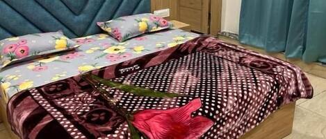 A bed with a wooden frame, a blue upholstered headboard, floral bedding, and a patterned throw.