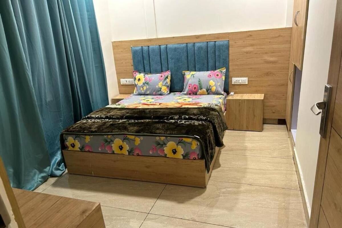 A bedroom with a wooden bed frame, a blue upholstered headboard, and floral-patterned bedding.