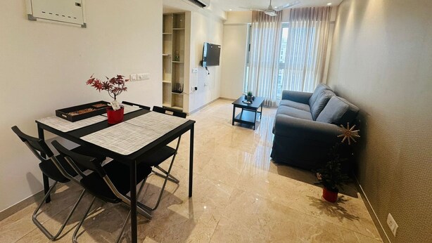 A modern living room with a sofa, a dining table with chairs, a small side table, and a potted plant.