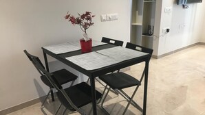 A dining area with a table set for four, surrounded by black chairs, a red vase with flowers, and a wall-mounted TV.