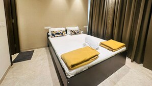 A modern hotel room with a large bed, two pillows, a bedside table, a ceiling fan, and a view of the outside through curtains.