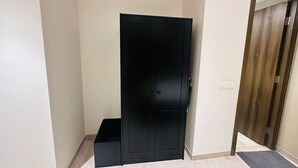 A room with a black wardrobe, a wooden door, a small black bench, and a tiled floor.