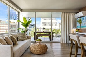 A modern living room with a sofa, a round woven ottoman, and a dining area with a table and chairs. - Waikiki Ocean View Retreat – Close to the Beach (Honolulu)