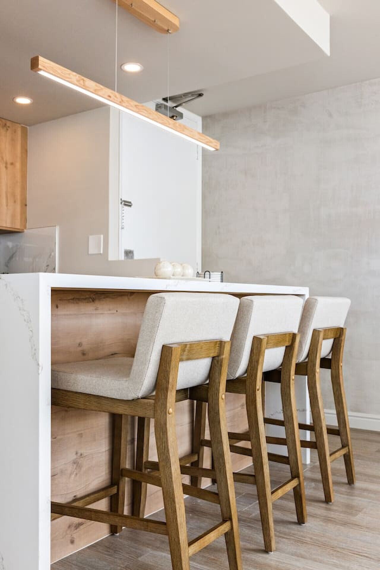 A modern kitchen with a wooden bar stool seating area, a white countertop, and a hanging light fixture.