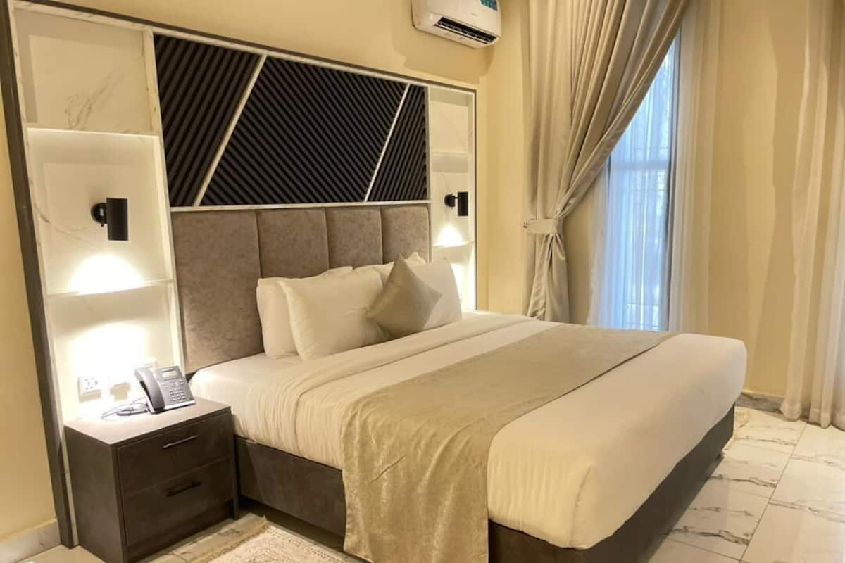 A modern bedroom with a large bed, bedside lamps, a nightstand, and a window with curtains.