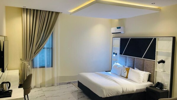 A hotel room with a bed, a desk, a chair, a TV, and an air conditioning unit. - Rhino suite Yola (Jimeta)