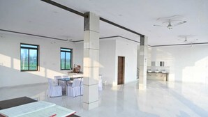 A spacious hotel room with a large window, a dining area with chairs and tables, and a kitchen area with sinks. - Hotel Raj Palace & Restaurant (Danta Ramgarh)
