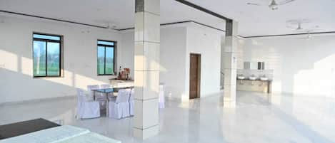 A spacious hotel room with a large window, a dining area with chairs and tables, and a kitchen area with sinks.