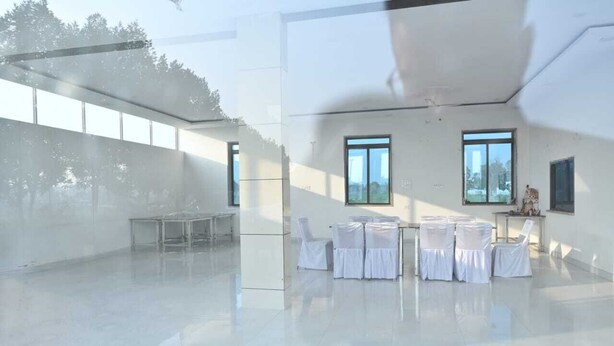 A spacious, modern indoor area with a large table and chairs, large windows, and a view of the outdoors. - Hotel Raj Palace & Restaurant (Danta Ramgarh)