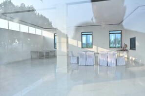 A spacious, modern indoor area with a large table and chairs, large windows, and a view of the outdoors. - Hotel Raj Palace & Restaurant (Danta Ramgarh)