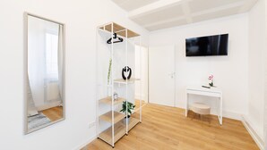 A modern, minimalist room with a wooden floor, white walls, a large mirror, a white desk with a plant, and a mounted TV. - Modern New 120m2 Apartment City Center KaDeWe /ZOO (Berlin)