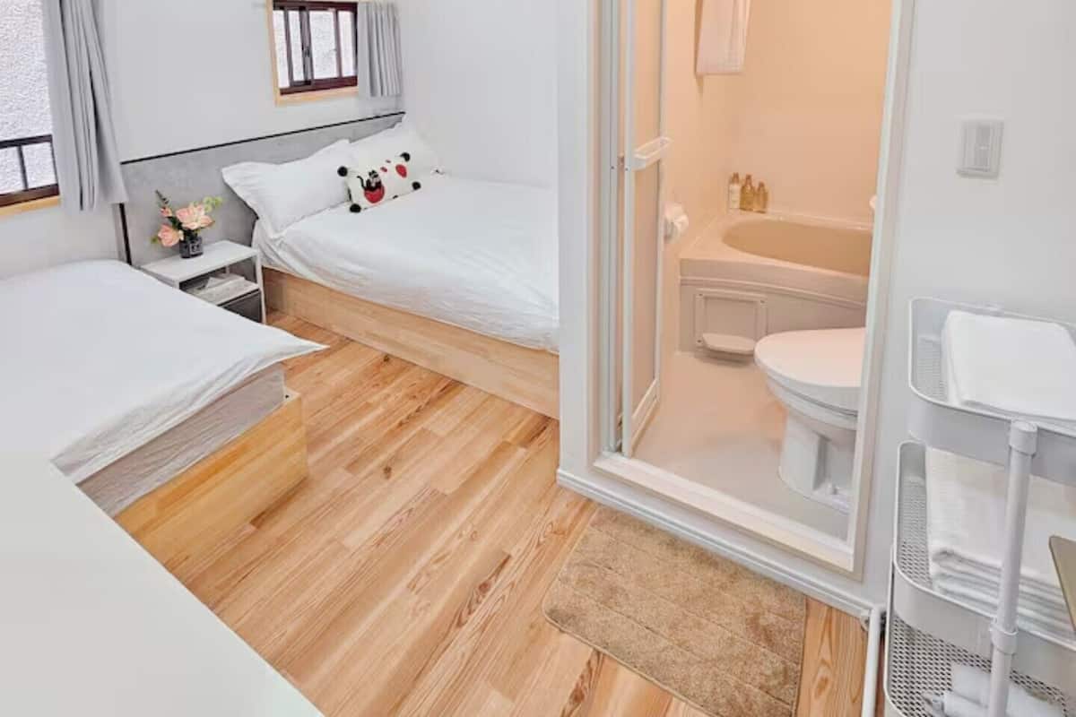 A modern hotel room with a bed, bedside table, and a bathroom visible through an open door.