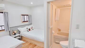 A modern hotel room with a bed, bedside table, and a bathroom visible through an open door.