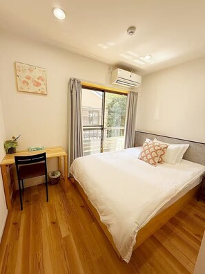 Une chambre à coucher comprenant un lit, un bureau, une chaise, un climatiseur et une fenêtre avec des rideaux.