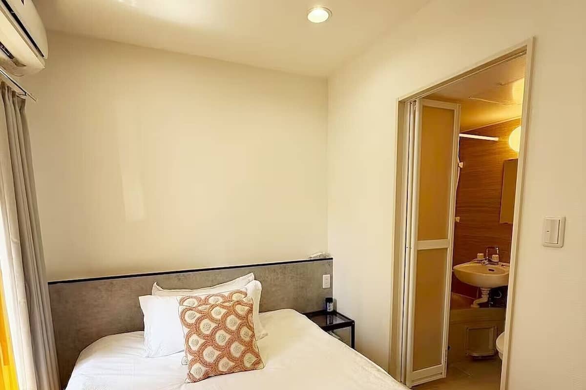 A hotel room with a bed, a nightstand, a mirror, and a bathroom visible through an open door.