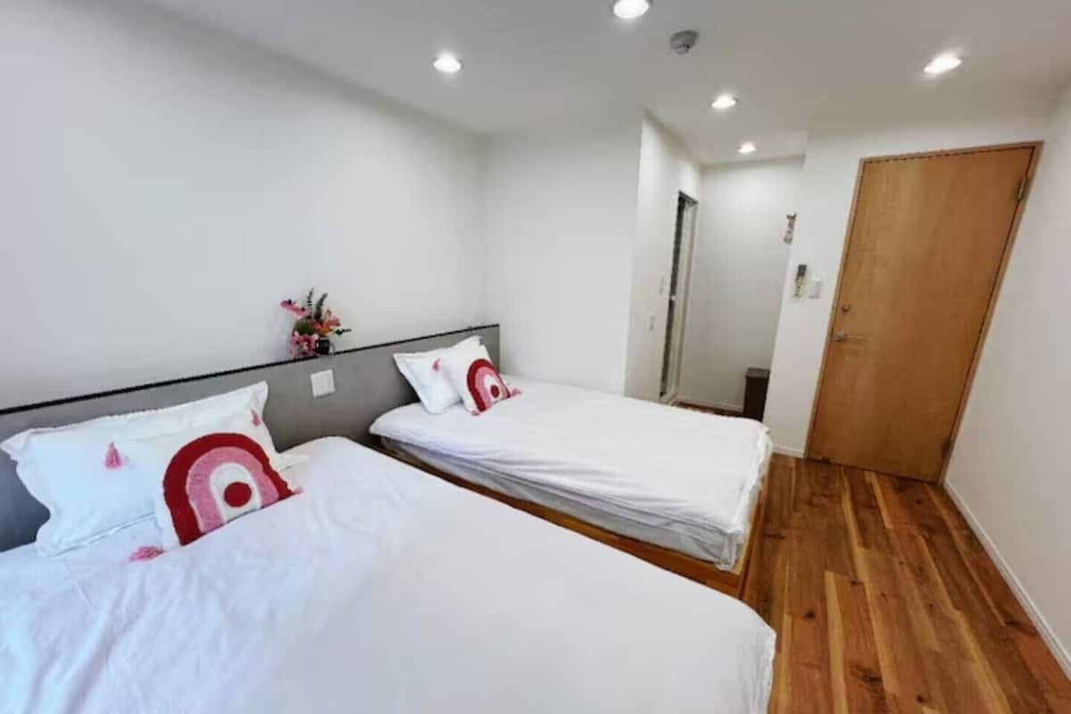 A room with two beds, a wooden floor, white walls, and a wooden door.