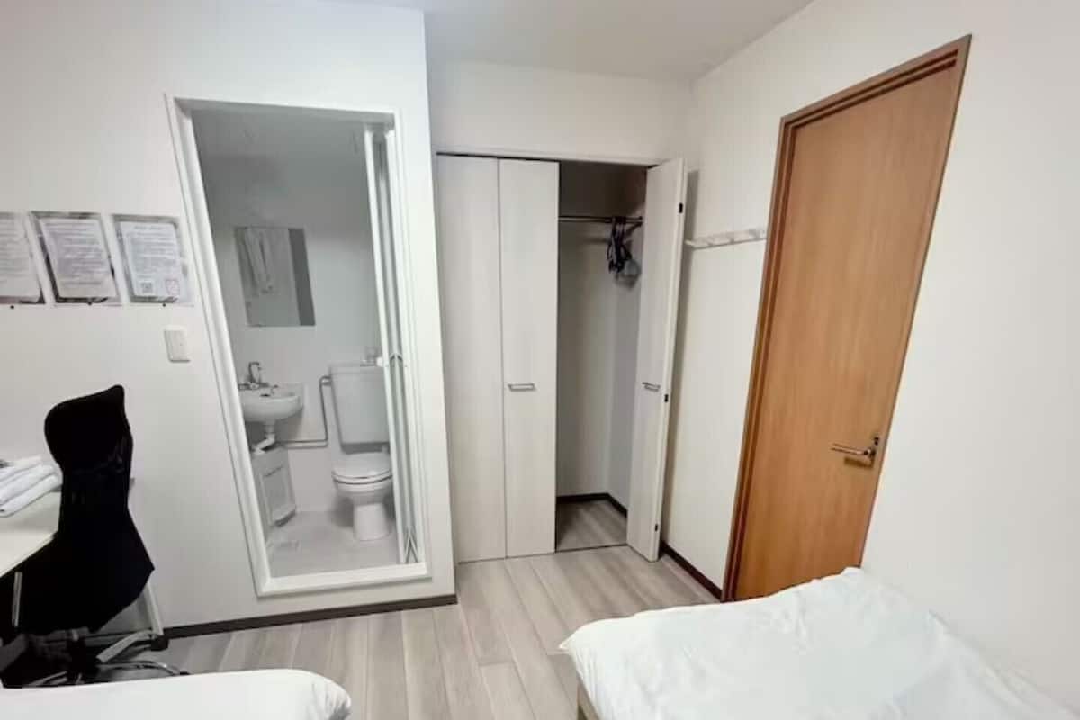 A bedroom with two beds, a desk, a chair, a wardrobe, and a bathroom.