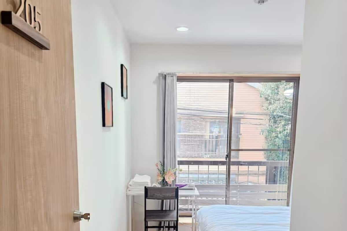 A bedroom with a bed, a desk with a chair, a window with curtains, and a door with a number.