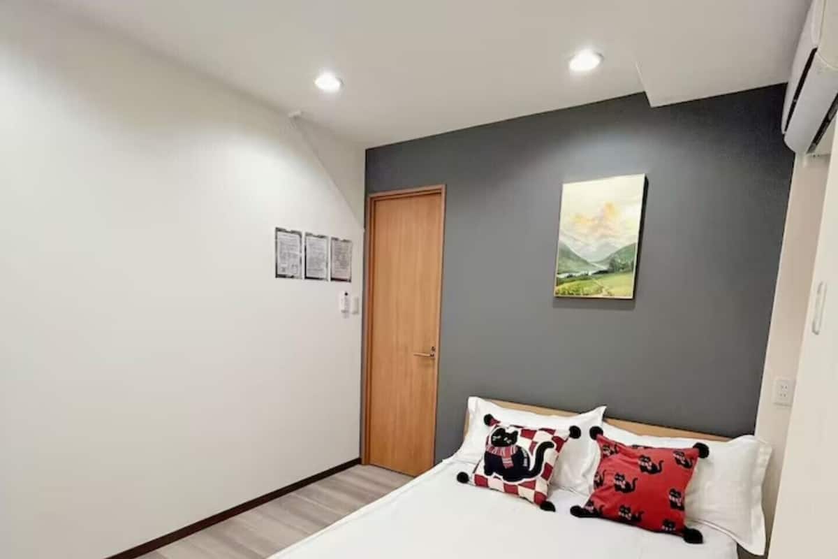 A bedroom with a bed, a wooden door, a painting on the wall, and a ceiling light.