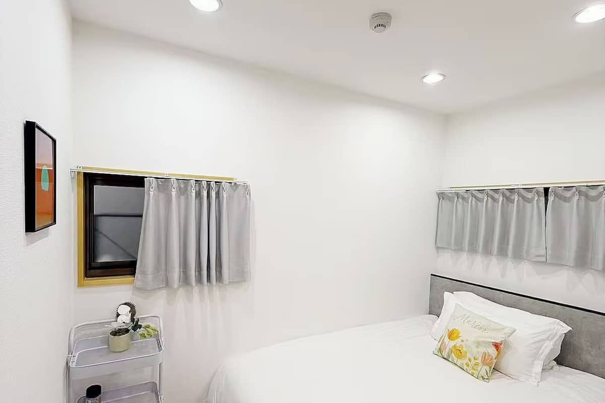 A bedroom with a bed, a window with curtains, a bedside table with a plant, and a headboard.
