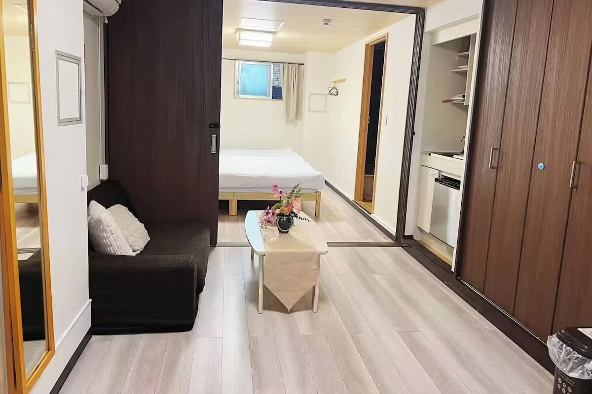A compact room with a bed, a small table with a vase, a wardrobe, and a mirror.
