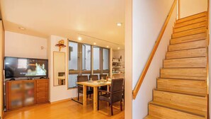 Un salon moderne avec un escalier en bois, un coin repas avec une table et des chaises, et un téléviseur posé sur un meuble en bois.